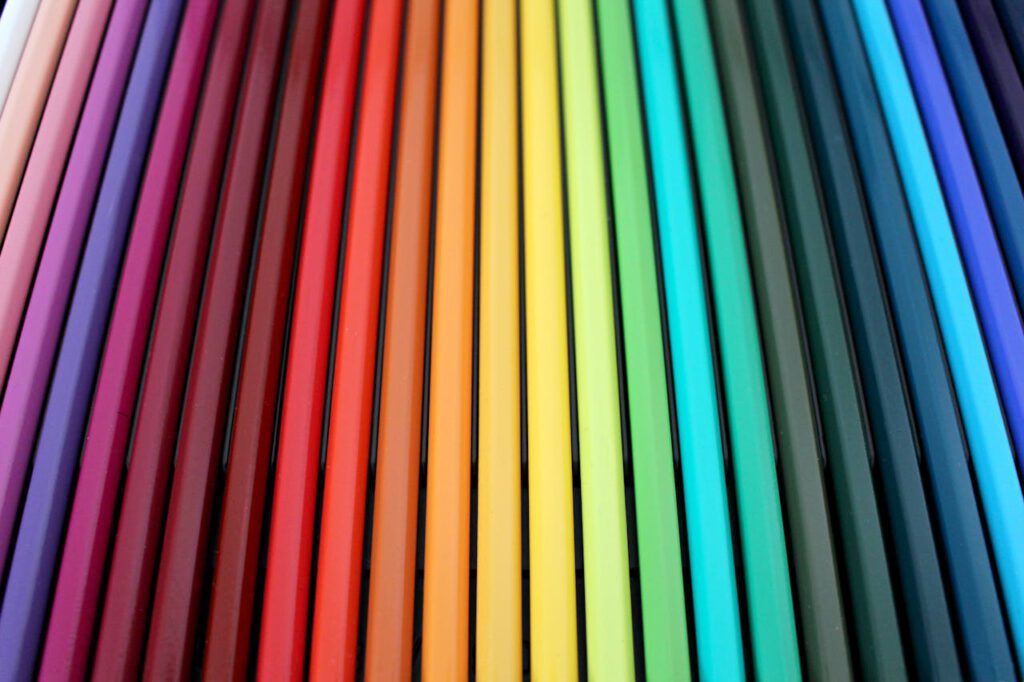 A vibrant and colorful arrangement of colored pencils forming a rainbow spectrum pattern.